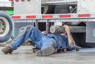Technician repairing a commercial trailer on a creeper